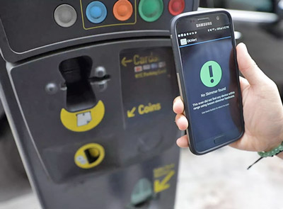 Phone being held up to credit card skimmer. 